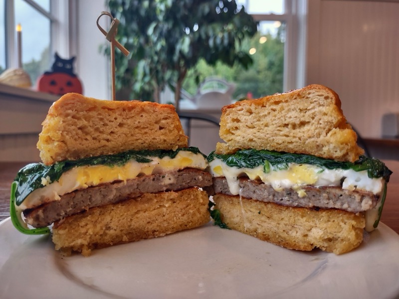 A biscuit sandwich with sausage, egg, cheese and spinach, cut in half