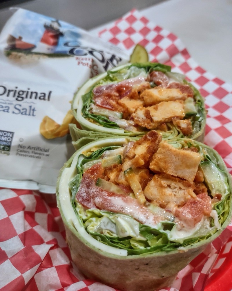 A Buffalo Chicken Wrap cut in half, with a bag of Cape Cod potato chips on red checked paper