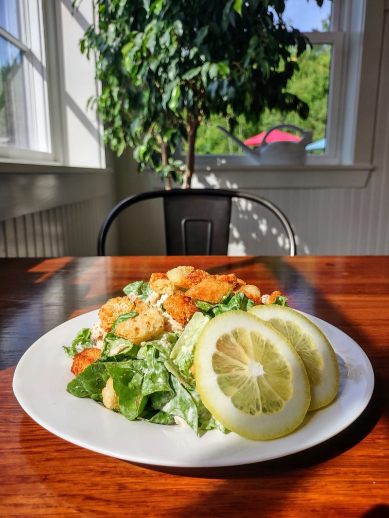 A Caesar salad with croutons and lemon slices on a sunny table