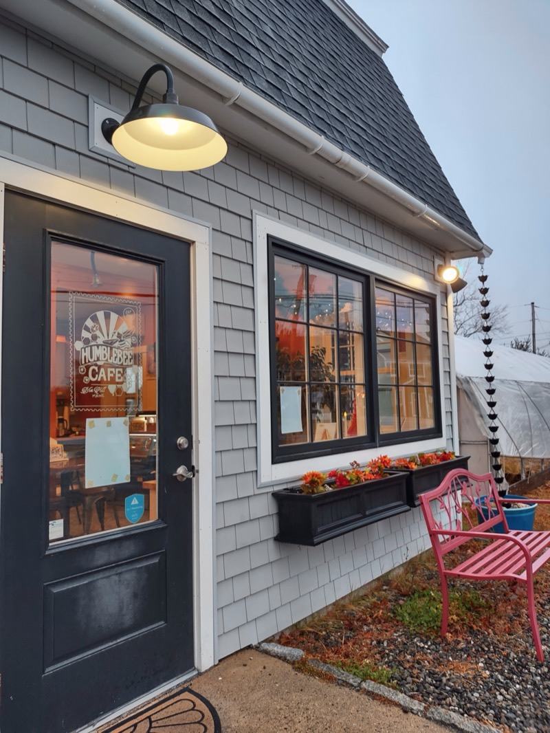 The black front door with the Humblebee Cafe logo on the glass, a barn light above and window boxes beside it