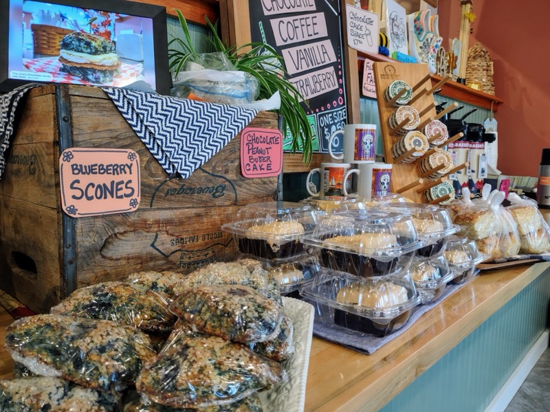 The counter with blueberry scones, wrapped treats and coffee mugs under hand-lettered signs