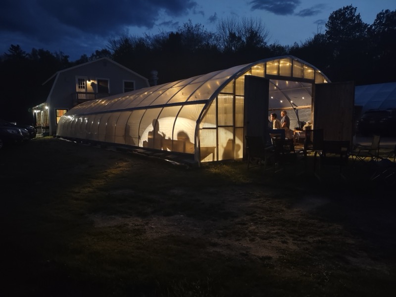 The greenhouse seating glowing at dusk, with people at tables inside