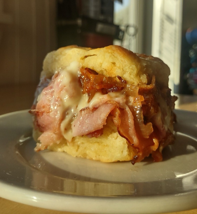 A grilled buttermilk biscuit sandwich with ham, melted Swiss cheese and a dark jam