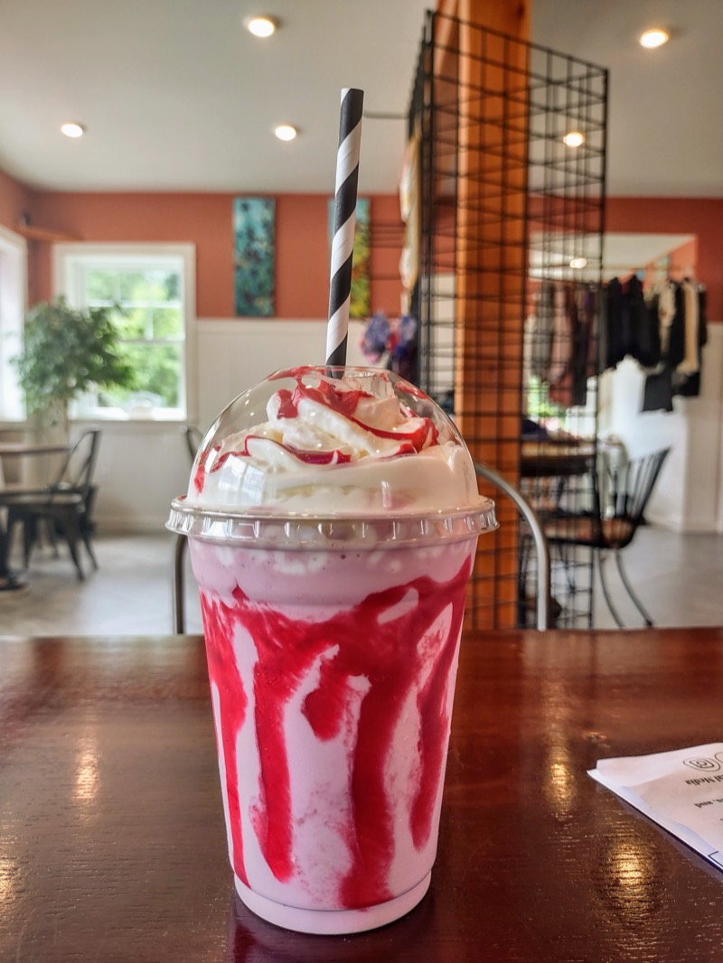 A strawberry milkshake with whipped cream and strawberry swirls, with the dining room behind it